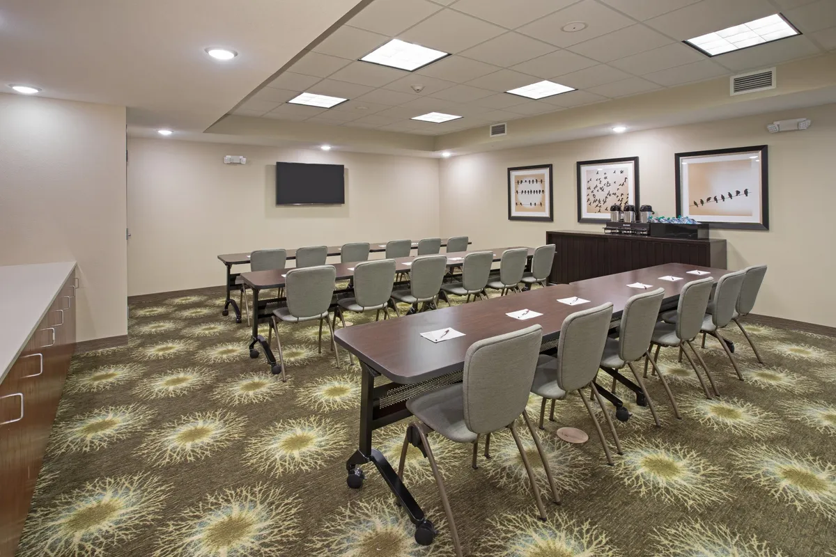 A stylish conference space with a long table surrounded by comfortable chairs, decorative wall art, and a large TV screen. The setting is perfect for team meetings, collaborative sessions, or informal gatherings, suggesting a flexible environment for both productivity and socializing after exploring the city.