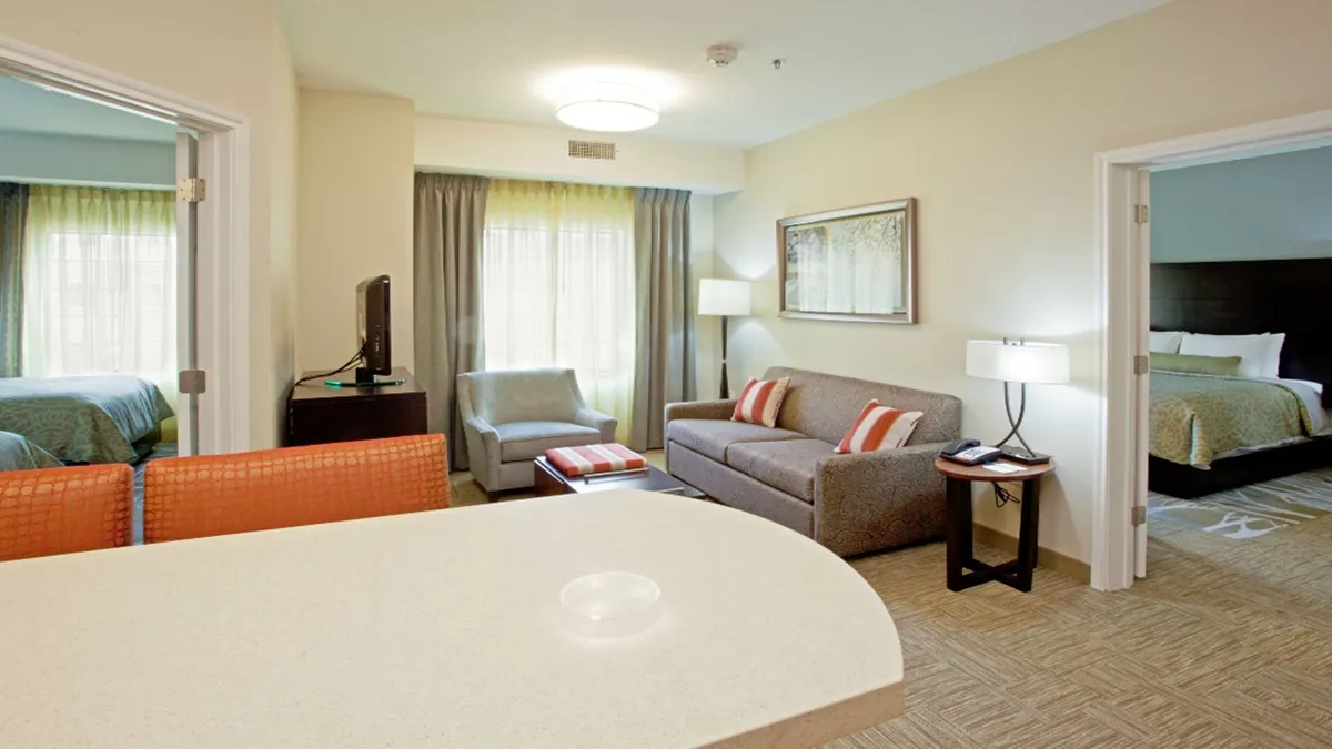 The image showcases a sun-filled living and dining area with a plush sofa adorned with decorative cushions, a stylish dining table set, and expansive windows that flood the space with natural light. Tasteful artwork adds a touch of personality, creating an inviting setting perfect for relaxing, sharing meals, or unwinding after a day of exploring Denver.