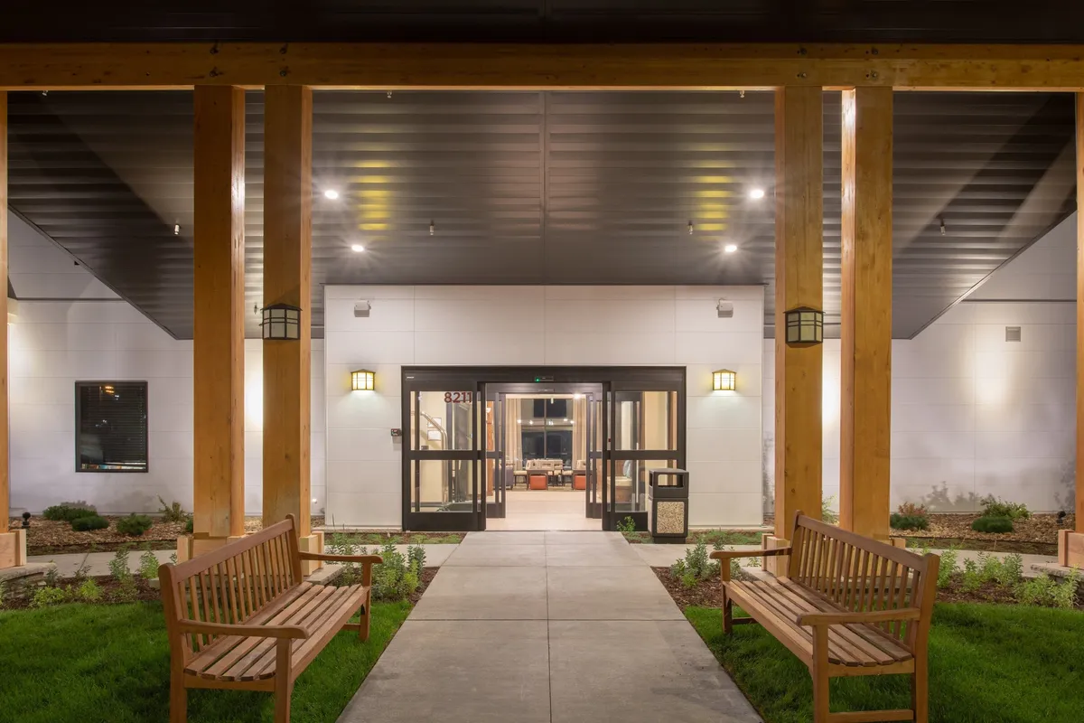 This image captures the inviting entrance doors to the property, flanked by wooden benches and lush landscaped greenery. The scene exudes a sense of welcome and comfort, signaling a thoughtfully maintained and accessible entry point for guests.