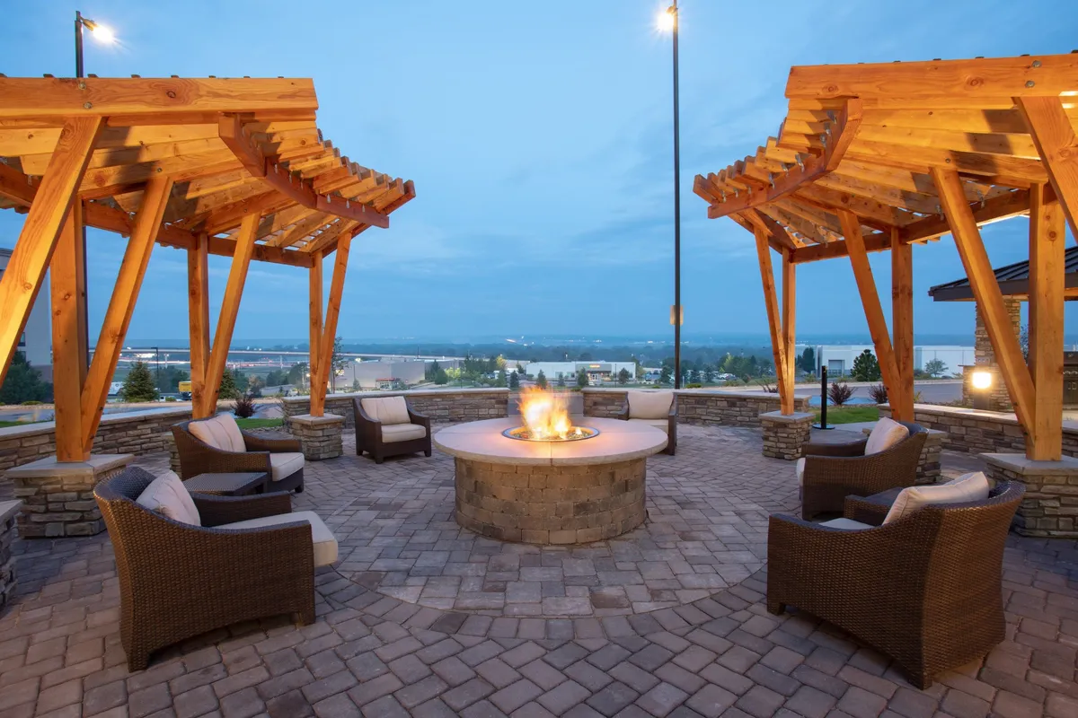 This exterior image features a cozy fire pit surrounded by wooden pergolas and comfortable lounge chairs, set against a backdrop perfect for socializing or enjoying a peaceful moment. The communal vibe is complemented by the warm lighting and relaxed outdoor seating, ideal for unwinding after a busy workday.