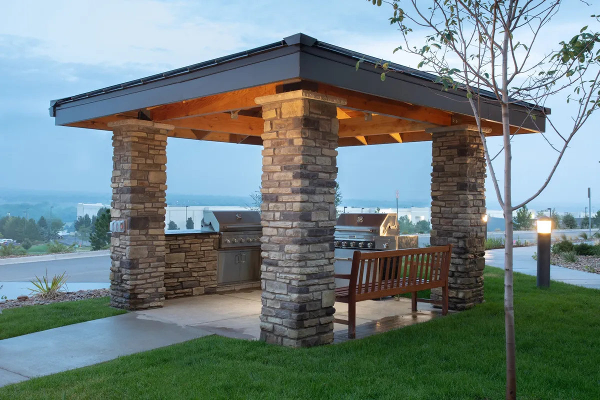 This scene captures a stone grill pavilion with benches, set in a landscaped area that offers a welcoming atmosphere for outdoor gatherings. The view suggests an ideal spot for sunset dinners or informal team celebrations, merging natural surroundings with hotel amenities.